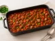 Herzhafter Partygulasch mit Fleisch, Paprika und Tomaten in großem Bräter auf weißem Holztisch