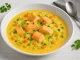 Lachssuppe mit Lachs, Gemüsewürfeln und Safran in einem tiefen Teller auf weißem Holzhintergrund