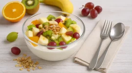 Glasschale mit Obstsalat und Quark, garniert mit Mandeln und frischen Früchten auf weißem Holztisch