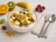 Glasschale mit Obstsalat und Quark, garniert mit Mandeln und frischen Früchten auf weißem Holztisch