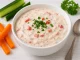 Quark-Tomaten-Dip mit Kräutern und Tomatenwürfeln in weißer Schüssel auf Holztisch