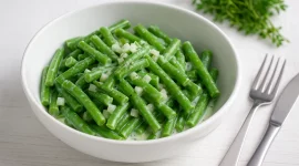 Bohnensalat aus grünen Bohnen mit saurer Sahne und Zwiebeln in weißer Schüssel auf Holztisch