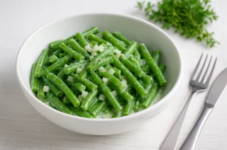 Bohnensalat aus grünen Bohnen mit saurer Sahne und Zwiebeln in weißer Schüssel auf Holztisch