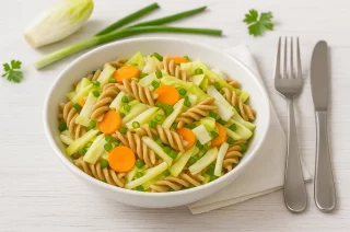 Schale mit Nudelsalat aus Chicorée, Möhren und Frühlingszwiebeln auf weißem Holzhintergrund