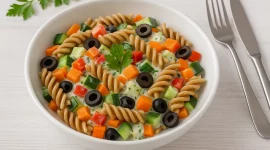 Bunter Nudelsalat mit Vollkornnudeln, Paprika, Karotten, Oliven und cremigem Lupinenjoghurt in Schüssel