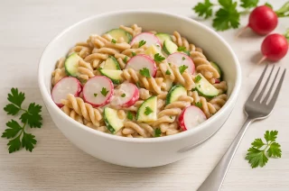Bunter Nudelsalat mit Radieschen, Zucchini und Nudeln in einer Schüssel auf hellem Holztisch angerichtet