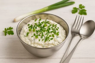 Schafskäsedip mit Quark, Schnittlauch und Frühlingszwiebeln in Edelstahlschale auf Holztisch