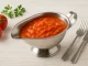 Tomaten-Zwiebel-Sauce in einer glänzenden Edelstahlsauciere, serviert auf Holztisch mit frischen Tomaten