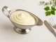 Cremige Mayonnaise ohne Ei in einer Edelstahl-Sauciere, serviert auf weißem Holzhintergrund mit moderner Deko