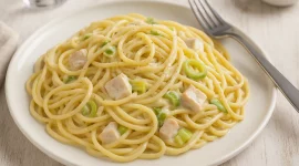 Spaghetti Carbonara mit Skyr, Hähnchenbrust und Lauch, serviert auf weißem Teller auf Holztisch