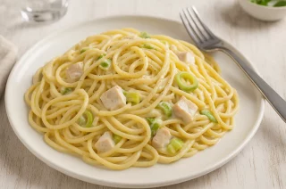 Spaghetti Carbonara mit Skyr, Hähnchenbrust und Lauch, serviert auf weißem Teller auf Holztisch