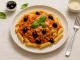 Penne mit Thunfischsugo, Oliven, Basilikum und Parmesan auf modernem Teller serviert