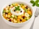 Obstsalat mit Äpfeln, Birne, Banane, Kiwi, Mandarinen und Skyr in einer weißen Schüssel auf hellem Holztisch