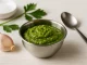 Grüner Knoblauchdip mit Kürbiskernmus, Knoblauch und Öl in einer Edelstahlschüssel auf weißem Holzhintergrund