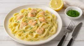 Bandnudeln mit cremiger Lachs-Sahne-Sauce und Kräutern auf weißem Teller serviert