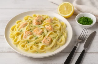 Bandnudeln mit cremiger Lachs-Sahne-Sauce und Kräutern auf weißem Teller serviert