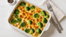 Brokkoli-Hähnchen-Gratin in einer Auflaufform, überbacken mit Käse und serviert auf weißem Holzhintergrund