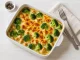Brokkoli-Hähnchen-Gratin in einer Auflaufform, überbacken mit Käse und serviert auf weißem Holzhintergrund