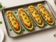 Gefüllte Zucchinihälften mit Hackfleisch und Käse überbacken, serviert auf weißem Holztisch