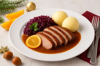 Geschmorte Entenbrust in Orangen-Soße mit Rotkohl und Kartoffelklößen auf festlichem Teller angerichtet