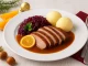 Geschmorte Entenbrust in Orangen-Soße mit Rotkohl und Kartoffelklößen auf festlichem Teller angerichtet