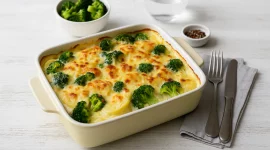 Kartoffel-Brokkoli-Auflauf in Auflaufform mit goldbrauner Käsekruste serviert auf weißem Holzhintergrund