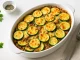 Zucchini-Hackfleisch-Gratin mit goldbraunem Käse überbacken in weißer Auflaufform auf Holztisch