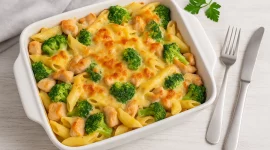 Hähnchen-Brokkoli-Nudelauflauf in einer Auflaufform, goldbraun mit Käse überbacken und serviert auf weißem Holzhintergrund