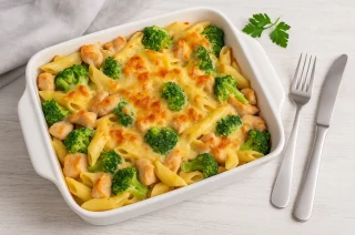 Hähnchen-Brokkoli-Nudelauflauf in einer Auflaufform, goldbraun mit Käse überbacken und serviert auf weißem Holzhintergrund