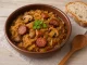 Teller mit polnischem Bigos, herzhaftem Eintopf aus Sauerkraut, Fleisch, Wurst und Pilzen, serviert mit Brot auf rustikalem Tisch