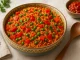 Bunte Schüssel Djuvec-Reis mit Paprika, Erbsen, Tomaten und Petersilie auf hellem Tisch