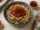 Bunte Schüssel Koshari mit Reis, Linsen, Nudeln, Tomatensoße und knusprigen Zwiebeln auf hellem Tisch