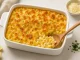 Amerikanisches Mac and Cheese mit goldbrauner Käsekruste in weißer Auflaufform, serviert mit Löffel auf hellem Tisch
