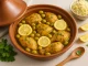 Tajine mit Hähnchen, grünen Oliven, eingelegten Zitronen und frischen Kräutern auf hellem Tisch