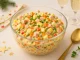 Bunter Silvestersalat mit Fleischwurst, Ei, Erbsen, Paprika und Mayonnaise-Dressing in Glasschale auf festlichem Tisch